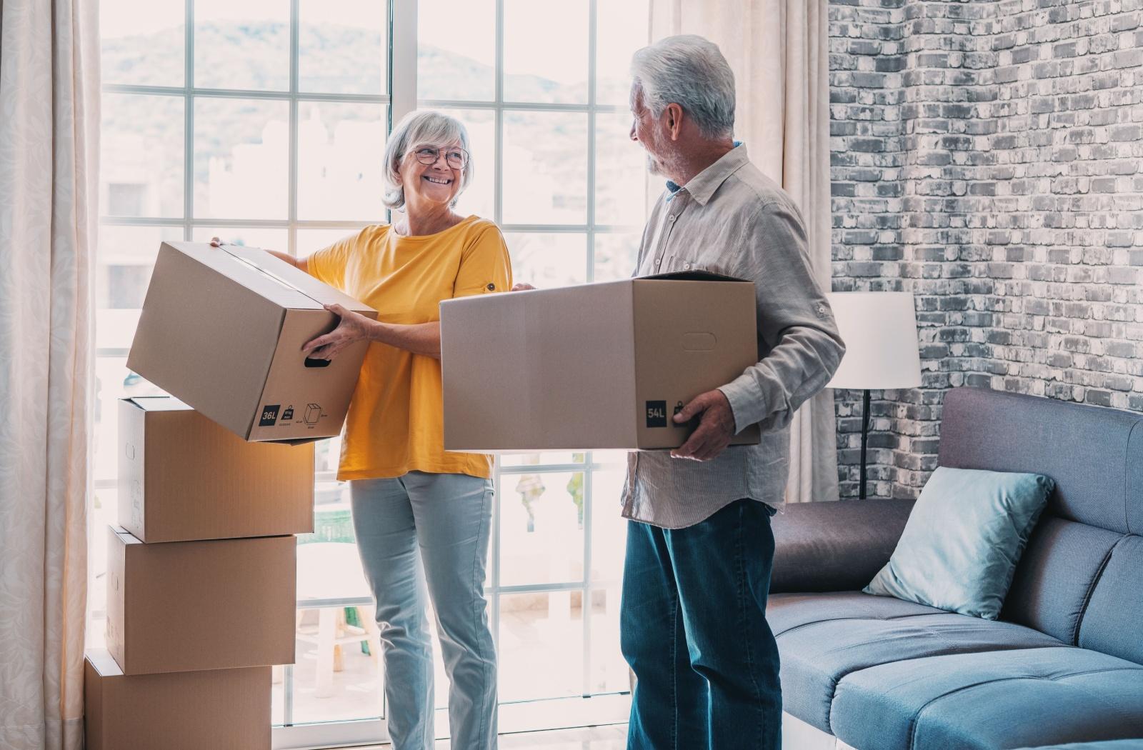A smiling older-adult couple stacks cardboard boxes as they downsize to move into a senior living community.